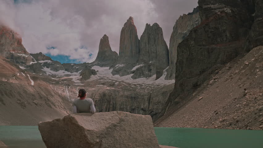 Woman sitting on a rock taking in the picturesque granite towers of Torres del Paine with parallax movement, Patagonia, Chile 