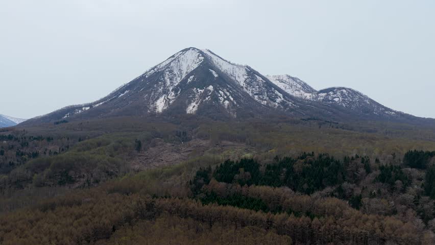 Aerial view of Mount Yotei with snow-capped peak rising above the dense forest landscape in Kyogoku, Hokkaido, Japan.