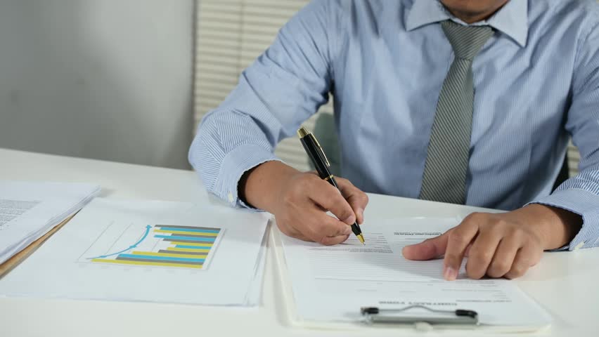 A businessman signs and submits contract documents on his desk.
