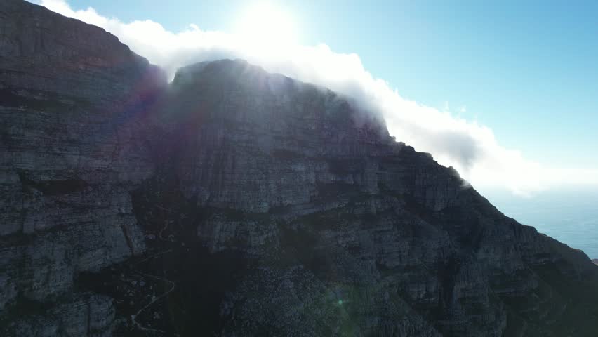White fog and clouds slowly roll down from the high mountains in Cape Town, South Africa, the sun shines through the clouds