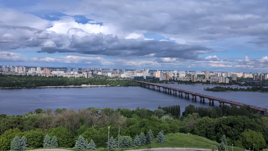 Panoramic scenic view of Kyiv left bank residential districts and Paton bridge across the wide Dnieper river under a cloudy summer sky