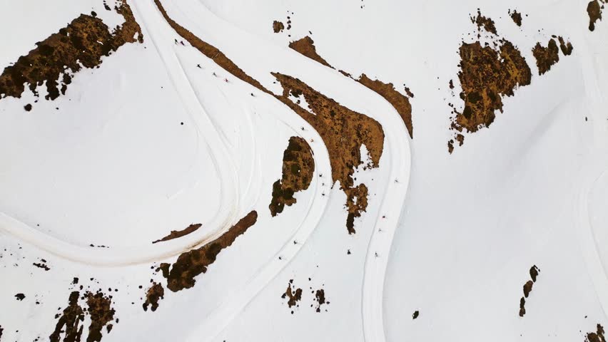 Amazing top down aerial view shows backcountry skiers and snowboarders climbing a snowy mountain slope on a winding trail in a minimalist and abstract winter landscape