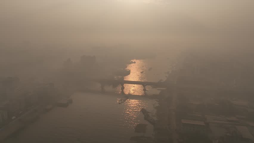 Aerial view of the Buriganga River at Sadarghat with boats navigating the hazy water under the golden sunset light in Dhaka, Dhaka Division, Bangladesh.