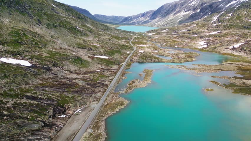 Aerial view of the historic Old Strynefjell Mountain Road winding through the rugged alpine landscape with turquoise glacial lakes and snow-capped peaks in Stryn Municipality, Vestland, Norway.