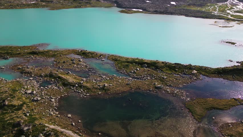 Aerial view of the turquoise glacial lake along the Old Strynefjell Mountain Road with rocky terrain and mossy patches in Stryn Municipality, Vestland, Norway.