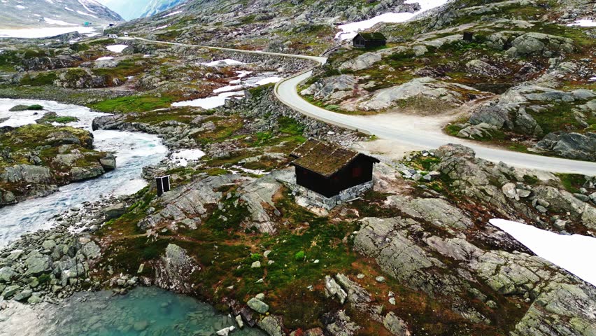 Aerial view of Old Strynefjell Mountain Road winding through the rocky landscape with a small cabin and a stream in Stryn Municipality, Vestland, Norway.