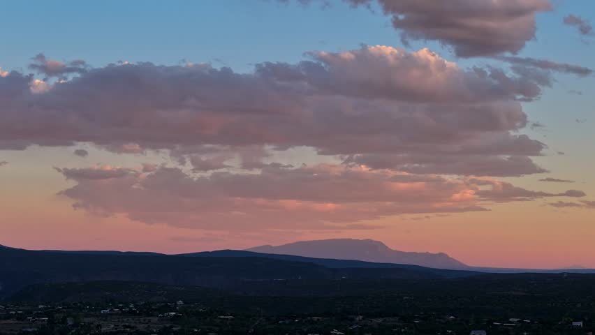 4K UHD drone timelapse capturing a vibrant sunset. Soft, textured clouds change from bright pink to deep purple over a sprawling desert town and the distant Sandia Mountains in New Mexico.