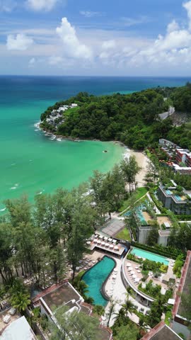 Aerial view of a luxury resort with swimming pools and lush trees nestled along the turquoise coastline of Phuket, Thailand.
