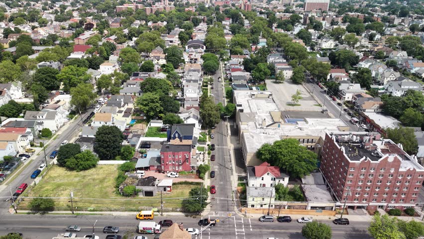 Aerial view flying backward along a street in a suburban american neighborhood, revealing the city skyline in the distance on a sunny day with green trees and residential houses below