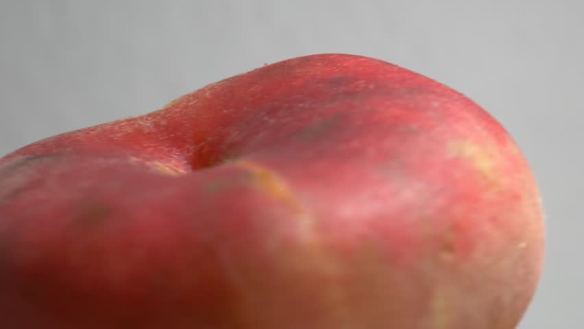 Close-up of fresh flat Saturn peaches rotating on a white plate, showcasing their fuzzy red skin and unique donut shape under bright studio lighting.