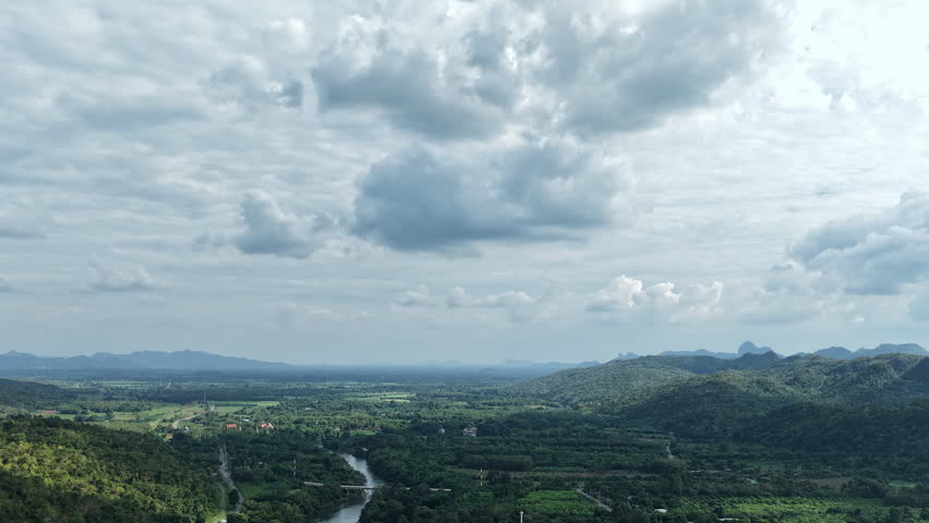 Expansive mountain landscape above Krasae River and train tracks under dramatic clouds in Thailand, drone aerial hyperlapse