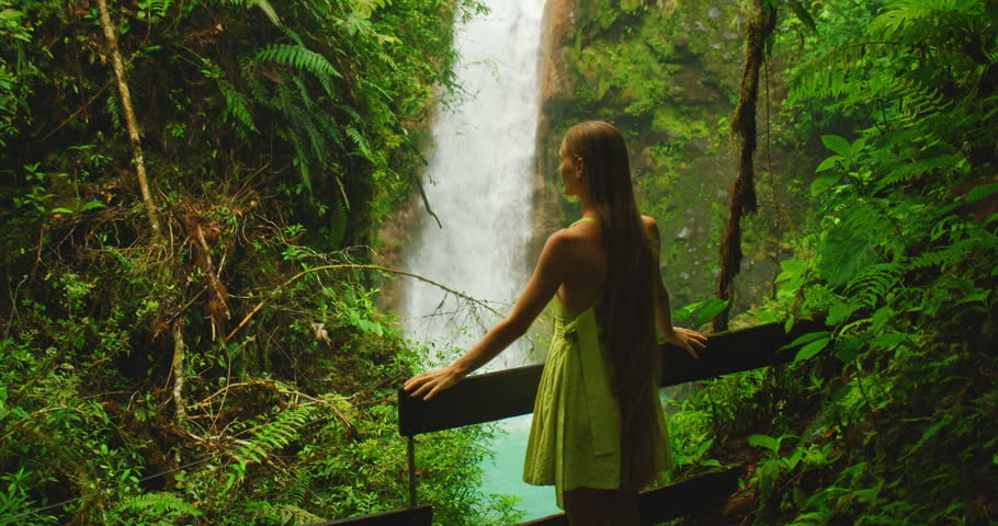 Tourist woman admiring a tall Pintada Waterfall from a jungle viewpoint during travel in Costa Rica