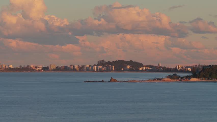 Aerial view of Currumbin Alley coastline with golden hour light reflecting on the ocean and distant city skyline in City of Gold Coast, Queensland, Australia.