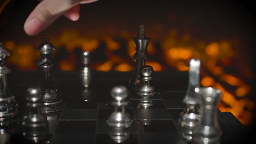 A wide view of silver chess pieces arranged on a chess board with dramatic warm orange fire-like lighting creating a cinematic atmosphere.