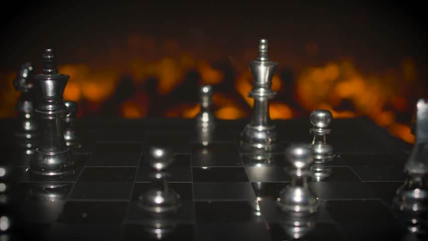 Silver chess pieces scattered and arranged on a chess board with dramatic warm orange lighting showing a mid-game position.