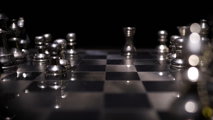 Silver chess pieces on a board in various positions with dramatic dark background and selective focus on key pieces.