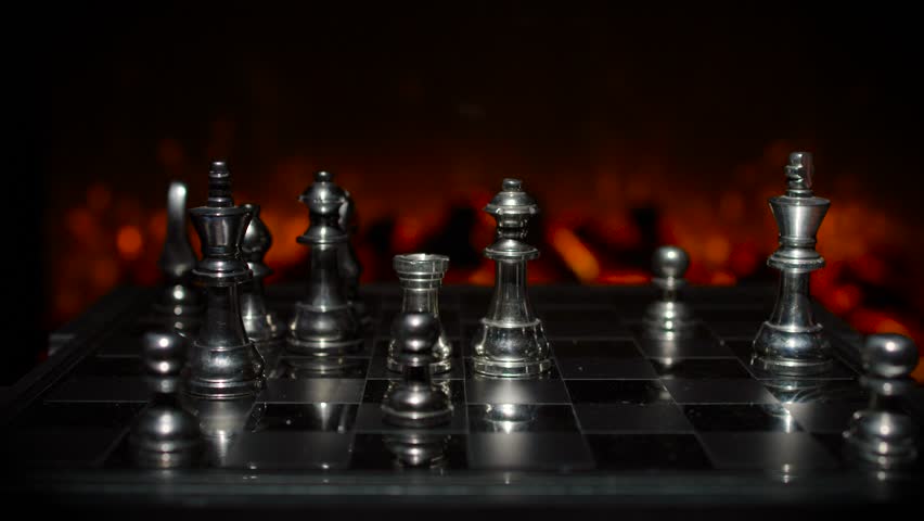 Silver chess pieces on a chess board in a tense arrangement with dramatic warm orange lighting and multiple pieces in play.