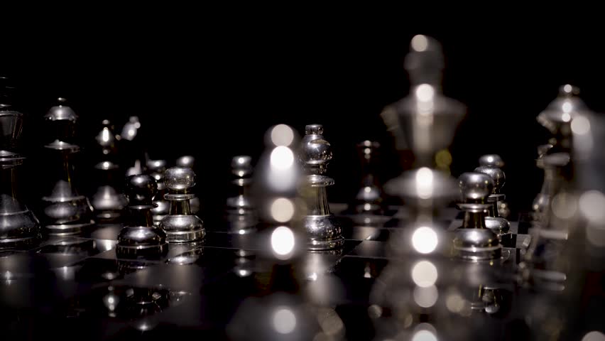 A close-up of silver chess pieces with the king piece highlighted against a dark background in a dramatic moody lighting.