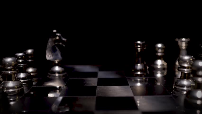 A close-up of silver chess pieces on a board in a complex mid-game position with dramatic dark background lighting.