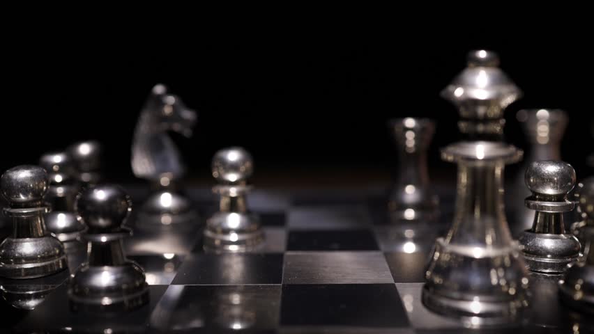 Silver chess pieces arranged in a game position on a chess board with soft bokeh lighting creating a blurred atmospheric background.