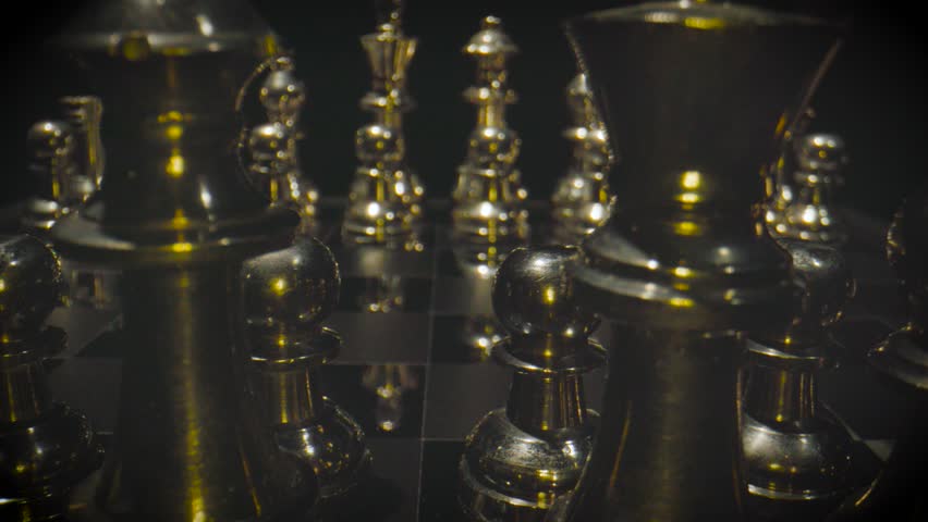 Golden and silver chess pieces arranged on a chess board with warm yellow and orange dramatic lighting in a luxurious setting.