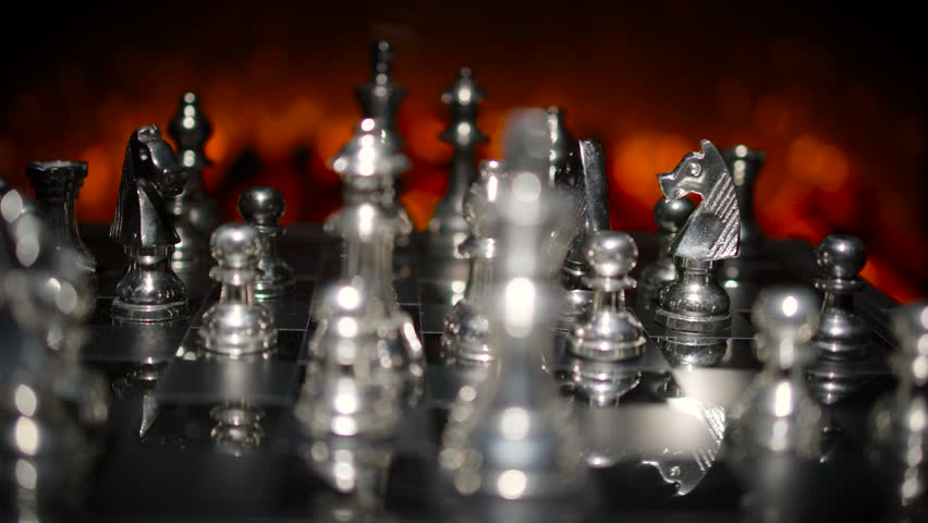 A wide view of golden chess pieces arranged on a chess board with dramatic warm orange lighting creating a rich cinematic scene.