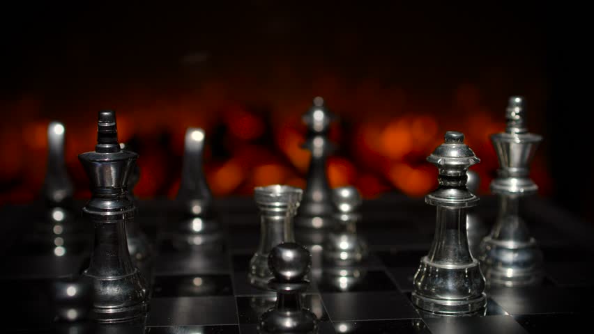 A close-up of silver chess pieces with dramatic dark background lighting creating depth and a moody cinematic atmosphere.