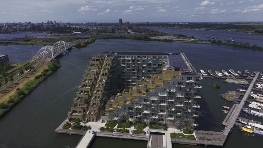 Aerial view of Sluishuis building with its unique cantilevered architecture, surrounding marina, and nearby bridge in Amsterdam, North Holland, Netherlands.