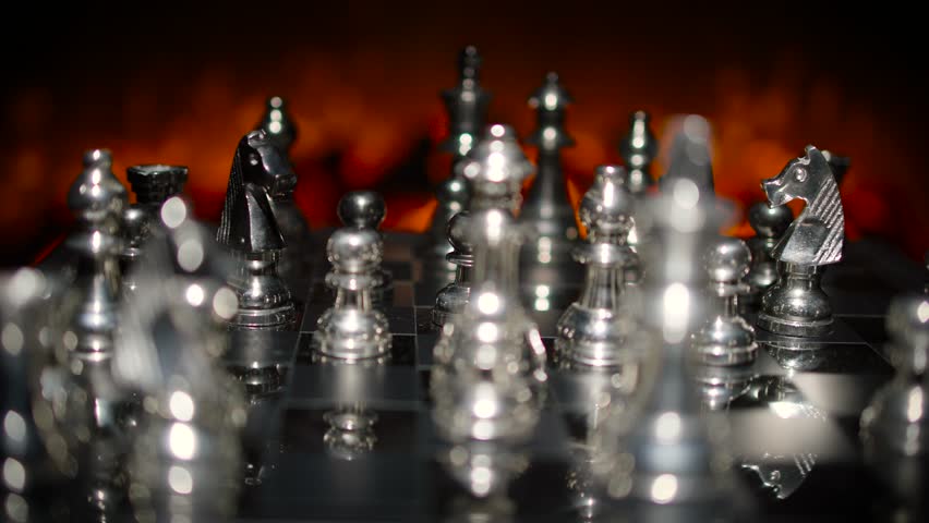 Silver chess pieces on a board with dramatic orange fire-like background lighting creating a powerful and intense atmosphere.