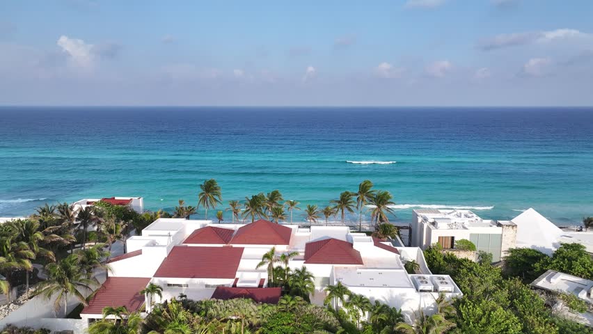Aerial view of a beach resort with red-tiled roofs and palm trees overlooking the turquoise Caribbean sea in Cancun, Quintana Roo, Mexico.