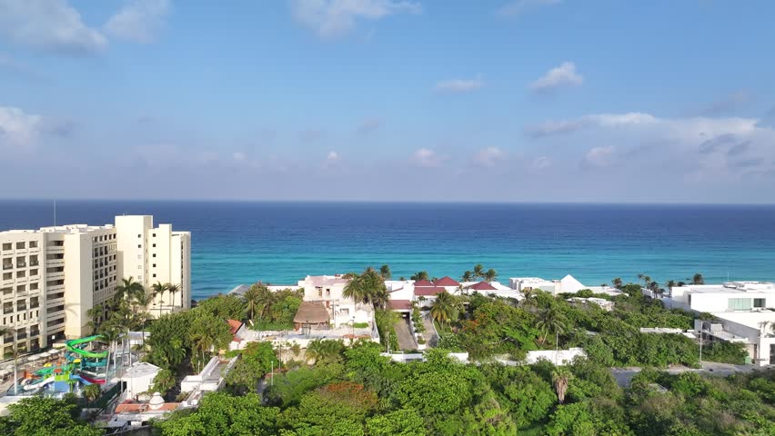 Aerial view of Cancun coastline with luxury resorts, lush tropical vegetation, and turquoise Caribbean Sea waters under a clear blue sky in Cancun, Quintana Roo, Mexico.