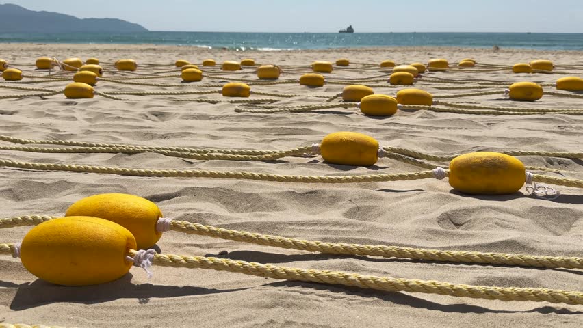 Close up of Yellow Beach Buoys Laid on Sand of the beach with Sea and Mountains in the Background