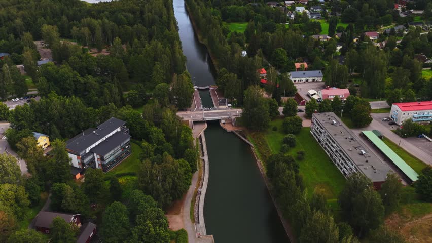 Aerial view of Vaaksy Canal with surrounding lush greenery, residential buildings, and a bridge crossing the waterway in Vaaksy, Paijat-Hame, Finland.