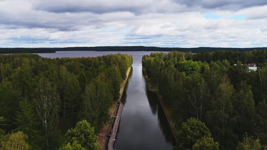 Aerial view of Vaaksy Canal flowing through dense green forests towards a large lake under a cloudy sky in Vaaksy, Paijat-Hame, Finland.
