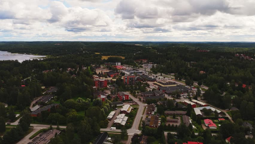 Aerial view of Vaaksy town with residential buildings, lush green forests, and nearby lake under a cloudy sky in Vaaksy, Paijat-Hame, Finland.