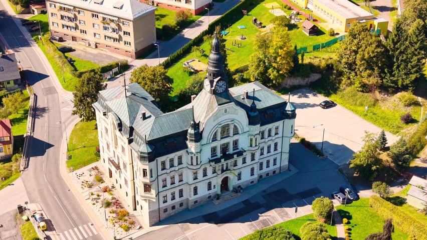 Aerial view of Tanvald Town Hall surrounded by green lawns and urban streets in Tanvald, Liberec Region, Czechia.