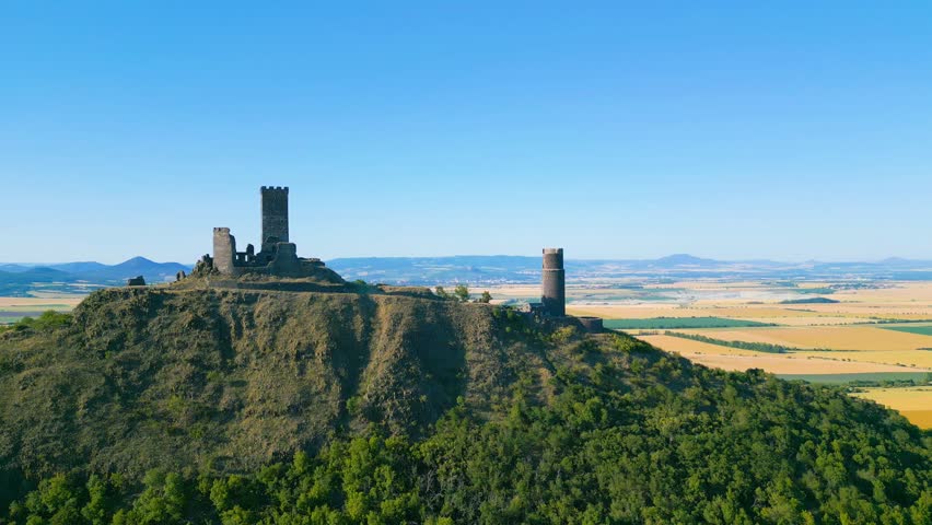 Aerial view of Hazmburk castle ruins on a hilltop with surrounding fields and clear blue sky in Klapy, Usti nad Labem Region, Czechia.