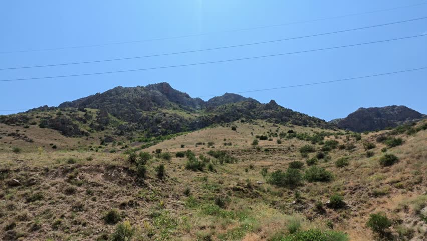 Dry grassy hills under clear blue sky. Rocky terrain with sparse green shrubs