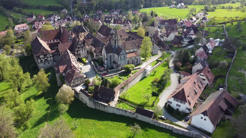Aerial view of the historic Bebenhausen Monastery complex with its timber-framed buildings and stone walls surrounded by lush green meadows in Tubingen, Baden-Wurttemberg, Germany.
