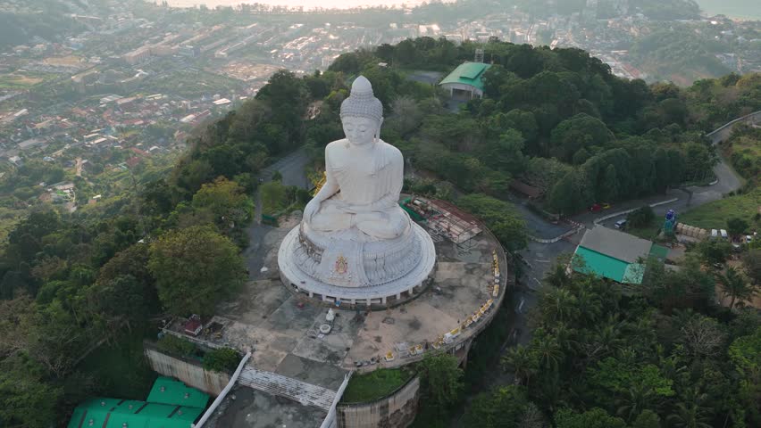 Aerial approach flyover past Big Buddha with Phuket coastline beyond at sunset, drone establishing city in backdrop