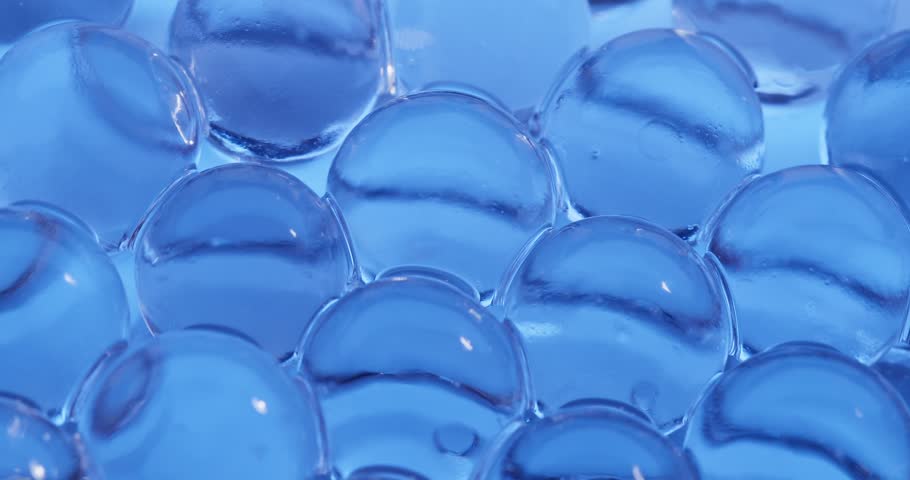 Panning close up across blue hydrogel water beads clustered on reflective surface, concept experimental with microscope for cell structure.