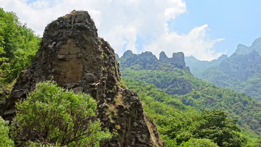 Rugged rock formations rise above lush green forests, creating a dramatic mountain landscape with natural textures and scenic wilderness