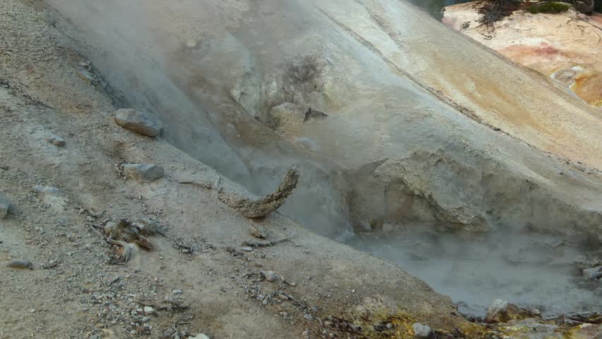 Static close up of steaming hydrothermal vent and mineral stained geothermal ground in Lassen Volcanic National Park, California, featuring active fumarole, sulfur deposits and volcanic terrain