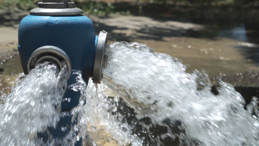 Close-up shot of a blue fire hydrant flushing out high-pressure water from its open side valves onto a street gutter. 4K slow motion 120 fps,