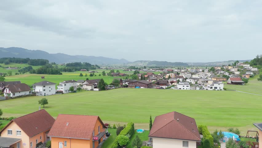 Aerial drone view of Kaltbrunn, Switzerland, showing a residential area beside open green fields and a rural village landscape.