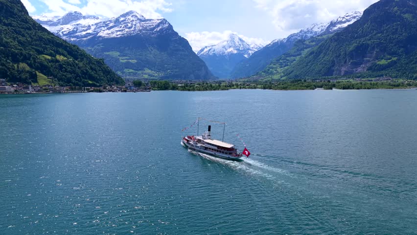 Aerial view of a historic paddle steamer cruising on Lake Lucerne with snow-capped mountains in the background in Fluelen, Uri, Switzerland.