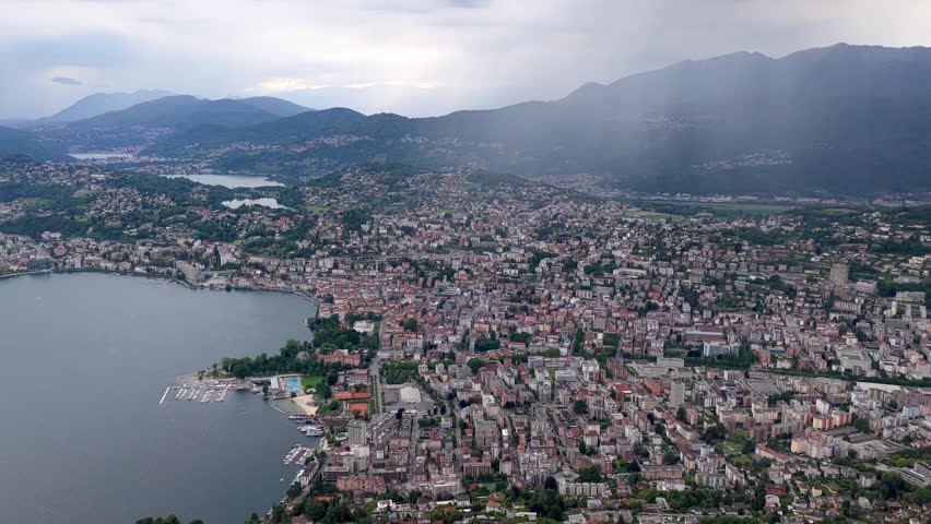 Aerial view of Monte Bre overlooking the dense urban landscape of Lugano nestled along the shores of Lake Lugano, with mountains in the background, Lugano, Ticino, Switzerland.