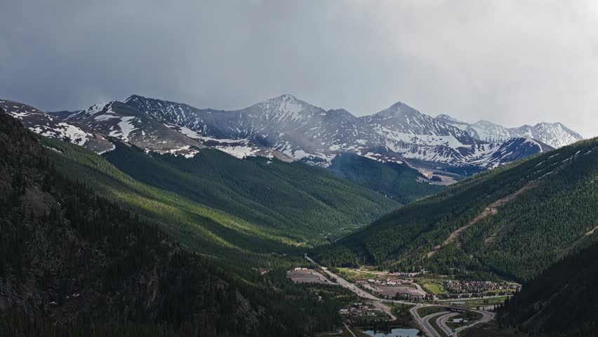 Forested mountain valley below snow capped alpine ridges, drone pullback reveals Wheeler Junction Colorado