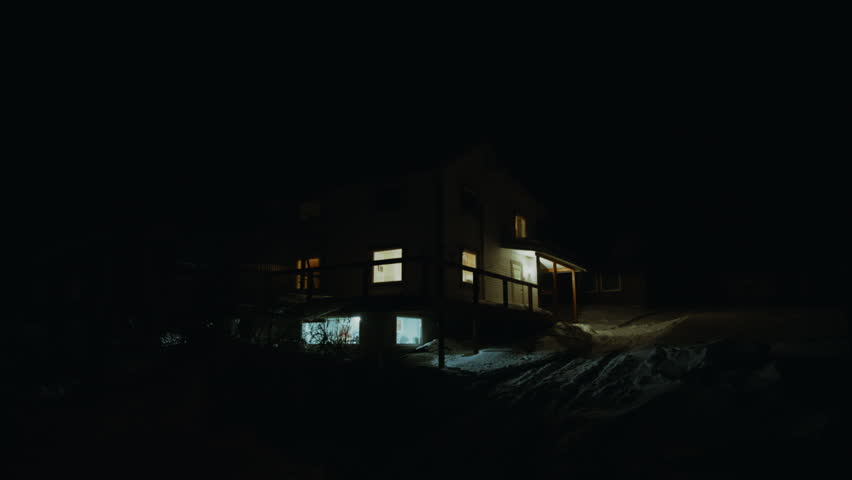 Lit house on snowy hillside at night in Arctic Norway with glowing windows and quiet winter setting, static medium