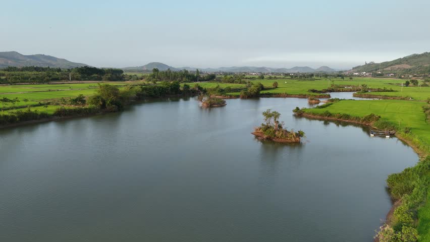 Drone footage flying across Bau Lon, a large man-made reservoir in Vietnam. Small islands of exposed land emerge from the water while a few distant boats drift quietly across the lake. The fading sunlight of sunset casts warm tones over the landscape, creating a peaceful and cinematic atmosphere as daylight comes to an end.